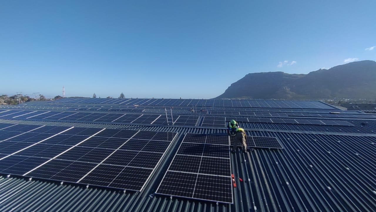 Technician inspecting a rooftop solar installation with mountains behind